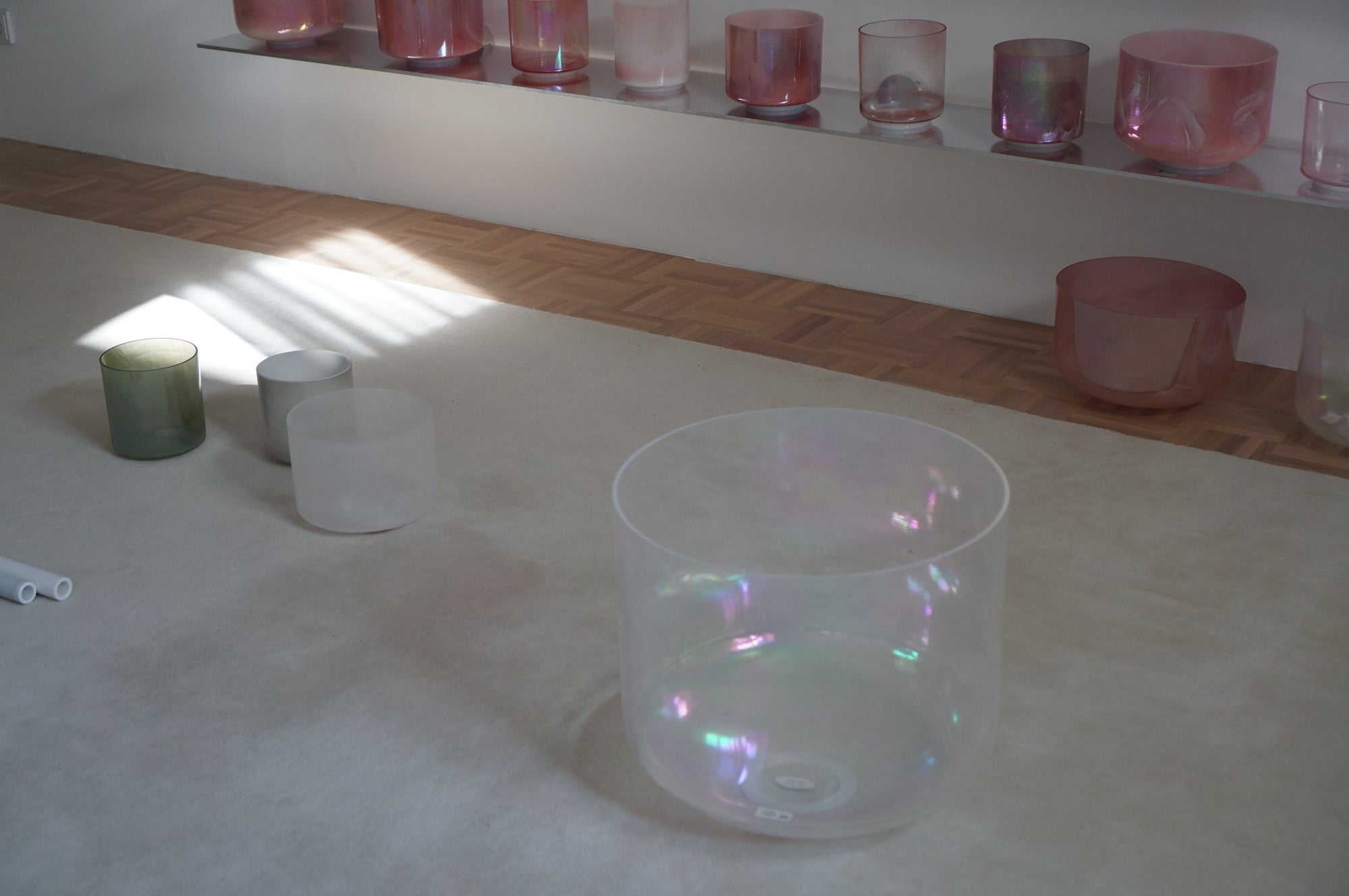 Transparent crystal tones singing bowls on a light-colored floor with pink singing bowls in the background.